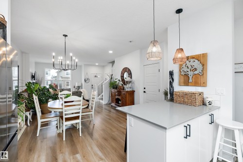 The open concept living area features light wood flooring, a modern chandelier over the dining space, and a kitchen island with a light-colored countertop and pendant lighting - 20 Hemingway Crescent, Spruce Grove, AB - Indoor