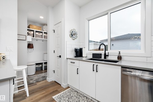 This modern space features white cabinetry, a black sink and faucet, a stainless steel dishwasher, and light-colored countertops - 20 Hemingway Crescent, Spruce Grove, AB - Indoor Photo Showing Kitchen With Double Sink