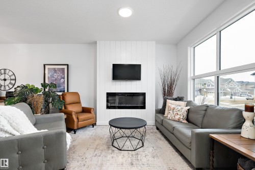 The living room features a fireplace with a white shiplap-style surround, large windows, and an overhead circular light fixture - 20 Hemingway Crescent, Spruce Grove, AB - Indoor Photo Showing Living Room With Fireplace