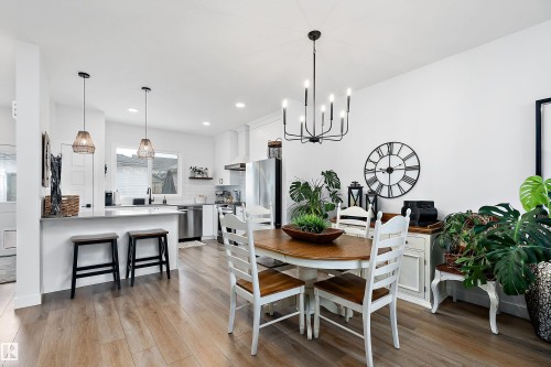 The property features an open-concept living area with light-toned flooring, a bright white kitchen with stainless steel appliances, and a dining space illuminated by a contemporary chandelier - 20 Hemingway Crescent, Spruce Grove, AB - Indoor Photo Showing Dining Room