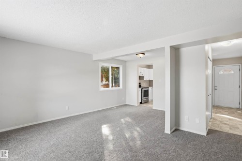 Spacious living area featuring light gray carpet flooring and a window providing natural light - 18297 74 Avenue, Edmonton, AB - Indoor Photo Showing Other Room