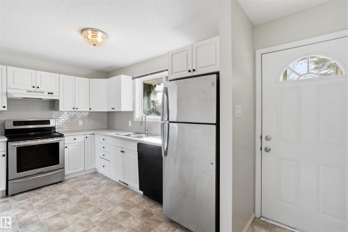 The kitchen features white cabinetry, stainless steel appliances, a tile backsplash, and a sink with a window view - 18297 74 Avenue, Edmonton, AB - Indoor Photo Showing Kitchen