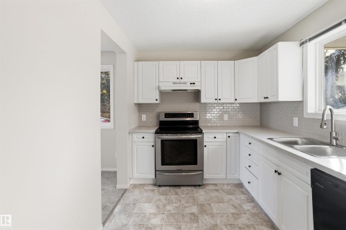 The kitchen features white cabinetry with black hardware, a stainless steel range, and a subway tile backsplash - 18297 74 Avenue, Edmonton, AB - Indoor Photo Showing Kitchen With Double Sink