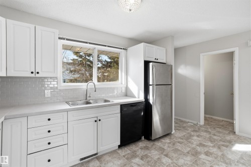 The kitchen features white cabinetry, a double basin sink, stainless steel appliances, and a tiled backsplash - 18297 74 Avenue, Edmonton, AB - Indoor Photo Showing Kitchen