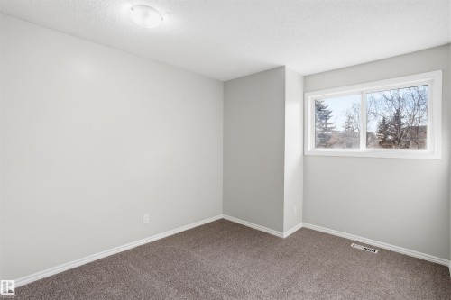 This room features neutral-toned walls, brown carpet, and a window providing natural light and a view of trees - 18297 74 Avenue, Edmonton, AB - Indoor Photo Showing Other Room