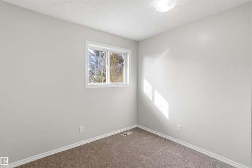 This room features light grey walls, brown carpeting, and a window with white trim providing natural light - 18297 74 Avenue, Edmonton, AB - Indoor Photo Showing Other Room