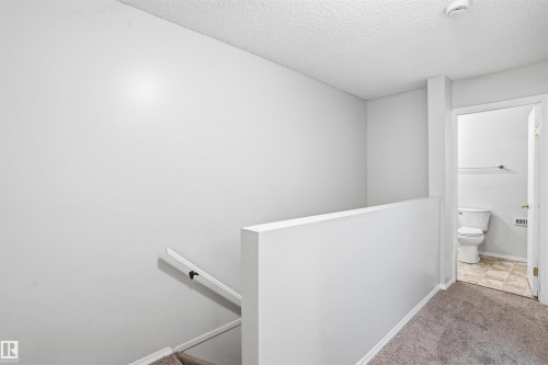 The property features a staircase with a white handrail, carpeted flooring, and a doorway leading to a bathroom with a toilet and tiled flooring - 18297 74 Avenue, Edmonton, AB - Indoor Photo Showing Other Room