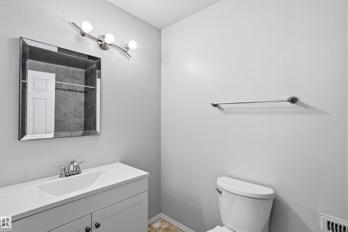 Bathroom featuring a white vanity with an integrated sink, a wall-mounted mirror, and a toilet - 18297 74 Avenue, Edmonton, AB - Indoor Photo Showing Bathroom