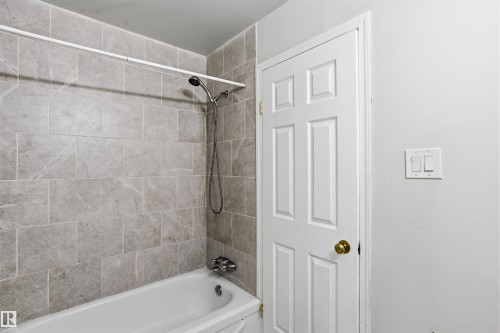 Bathroom featuring a white bathtub with a shower head, and light grey tiled walls - 18297 74 Avenue, Edmonton, AB - Indoor Photo Showing Bathroom