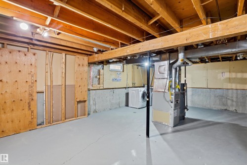 The property features an unfinished basement with exposed wooden beams, a painted concrete floor, and a washer and dryer - 18297 74 Avenue, Edmonton, AB - Indoor Photo Showing Basement