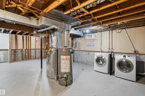 The unfinished basement features exposed wooden joists, concrete walls, a water heater, furnace, and a washer and dryer - 18297 74 Avenue, Edmonton, AB - Indoor