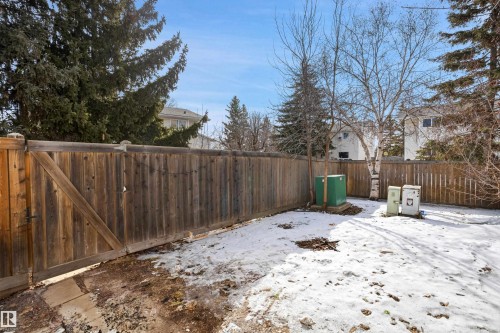 The property includes a spacious yard featuring a wooden fence, mature trees, and a clear blue sky overhead - 18297 74 Avenue, Edmonton, AB - Outdoor