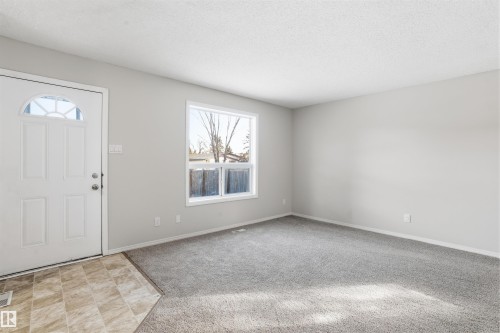 Entryway and living area featuring a white front door with an arched window, a large window providing natural light, and grey carpet flooring - 18297 74 Avenue, Edmonton, AB - Indoor Photo Showing Other Room