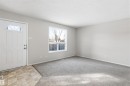 Entryway and living area featuring a white front door with an arched window, a large window providing natural light, and grey carpet flooring - 18297 74 Avenue, Edmonton, AB  - Indoor Photo Showing Other Room 