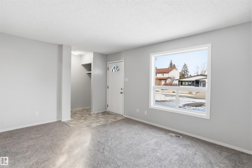 The property features light gray walls, gray carpeting, and a white front entry door with a decorative glass insert - 18297 74 Avenue, Edmonton, AB - Indoor Photo Showing Other Room