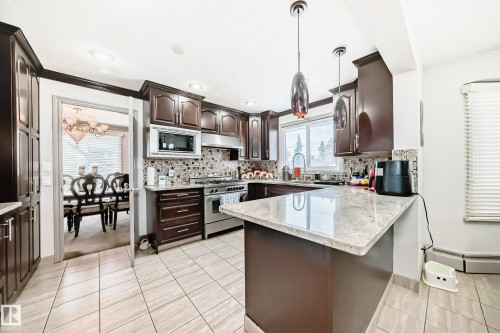 The kitchen features dark wood cabinetry, a light-colored granite countertop, and tiled flooring - 12131 101 Street Nw, Edmonton, AB - Indoor Photo Showing Kitchen With Upgraded Kitchen