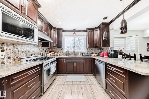 The kitchen features dark wood cabinetry, stainless steel appliances, a tiled backsplash, and granite countertops - 12131 101 Street Nw, Edmonton, AB - Indoor Photo Showing Kitchen With Upgraded Kitchen
