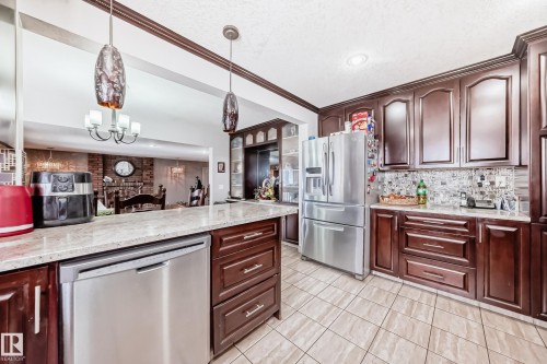 The kitchen features dark wood cabinetry, stainless steel appliances, light-colored countertops, and tiled flooring - 12131 101 Street Nw, Edmonton, AB - Indoor Photo Showing Kitchen