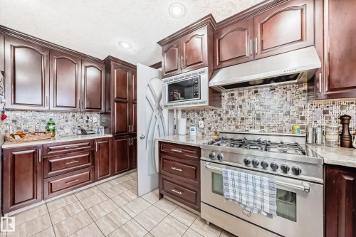 The kitchen features dark wood cabinetry, light-toned countertops, and a full stainless steel range with a matching range hood - 12131 101 Street Nw, Edmonton, AB - Indoor Photo Showing Kitchen With Upgraded Kitchen