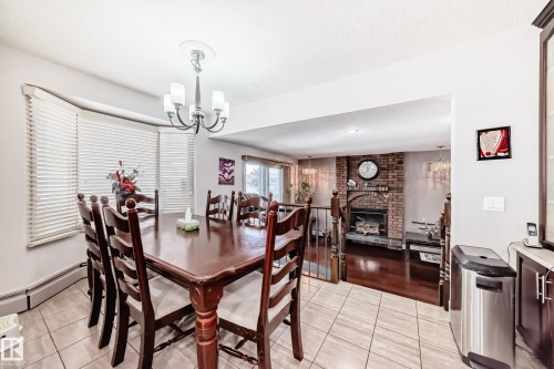 The dining area features tiled flooring, a bay window with blinds, and an overhead chandelier, providing a bright and inviting space - 12131 101 Street Nw, Edmonton, AB - Indoor Photo Showing Dining Room With Fireplace