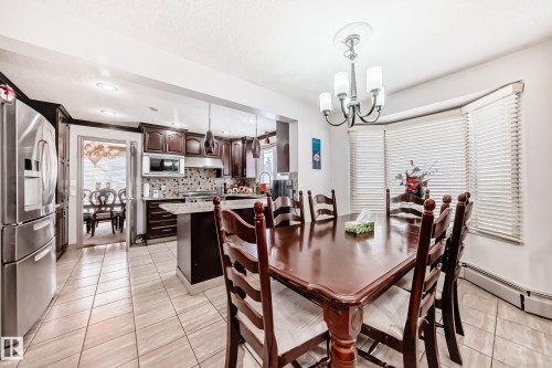 This open-concept area features a kitchen with dark wood cabinetry, stainless steel appliances, and a tiled backsplash - 12131 101 Street Nw, Edmonton, AB - Indoor Photo Showing Dining Room