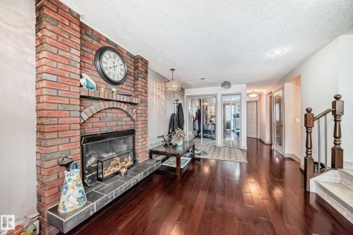 The interior features rich hardwood flooring, a brick fireplace with a hearth, and a staircase with wooden banisters - 12131 101 Street Nw, Edmonton, AB - Indoor Photo Showing Living Room With Fireplace