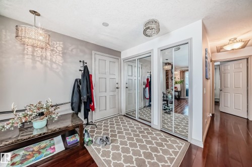 Inviting entryway featuring hardwood floors, a decorative ceiling light fixture, and two mirrored closet doors - 12131 101 Street Nw, Edmonton, AB - Indoor Photo Showing Other Room