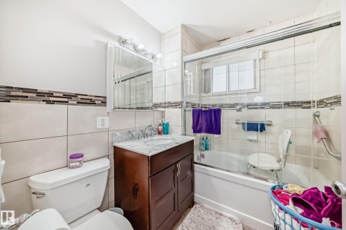 The bathroom features tiled walls with a decorative accent band, a vanity with a marble countertop, and a shower-bathtub combination with a glass enclosure - 12131 101 Street Nw, Edmonton, AB - Indoor Photo Showing Bathroom