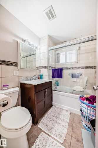 The bathroom features a vanity with a dark wood cabinet and a stone countertop, a toilet, and a bathtub with a clear glass shower enclosure - 12131 101 Street Nw, Edmonton, AB - Indoor Photo Showing Bathroom