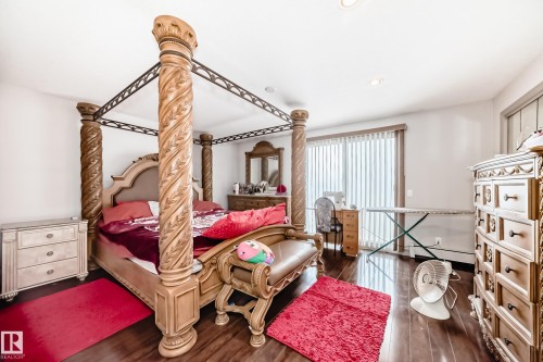 This bedroom features dark hardwood floors and a sliding glass door with vertical blinds - 12131 101 Street Nw, Edmonton, AB - Indoor