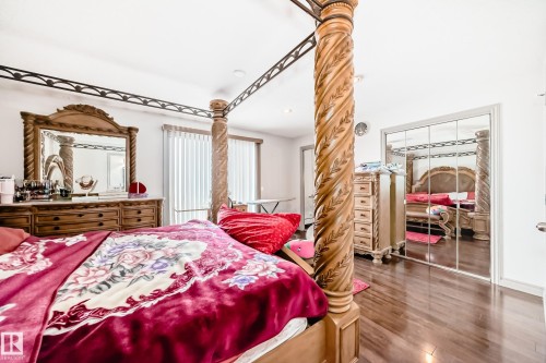 Bedroom featuring hardwood floors, a decorative wooden bed frame, a mirrored closet, and a wooden dresser with a mirror - 12131 101 Street Nw, Edmonton, AB - Indoor Photo Showing Bedroom