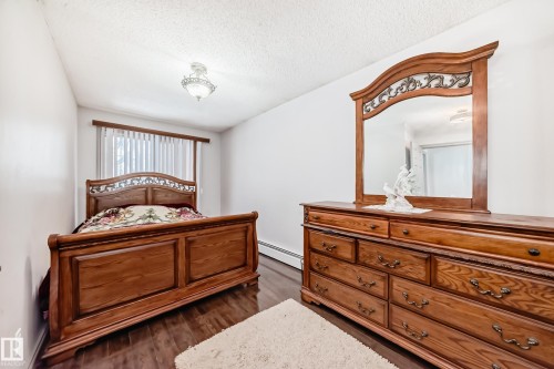 The room features rich hardwood flooring, a ceiling-mounted light fixture, and a window with vertical blinds - 12131 101 Street Nw, Edmonton, AB - Indoor Photo Showing Bedroom