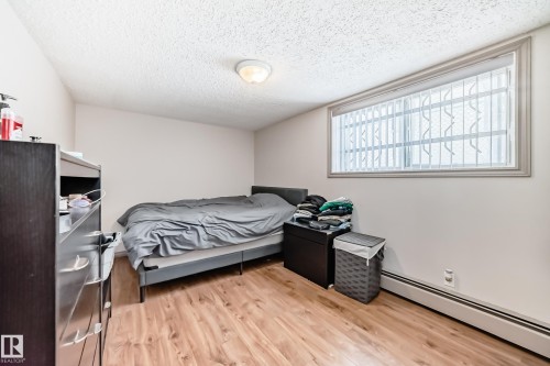 The room features wood-look flooring, light-colored walls, and a window with blinds - 12131 101 Street Nw, Edmonton, AB - Indoor Photo Showing Bedroom