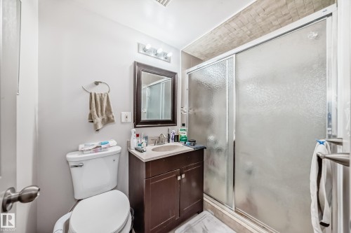 Bathroom featuring a vanity with a dark wood base and light-colored countertop, a framed mirror, and a shower with frosted sliding glass doors - 12131 101 Street Nw, Edmonton, AB - Indoor Photo Showing Bathroom