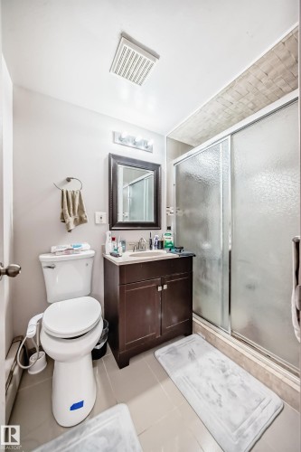 The bathroom features a vanity with a dark wood cabinet, a white toilet, and a stand-up shower with frosted glass doors - 12131 101 Street Nw, Edmonton, AB - Indoor Photo Showing Bathroom