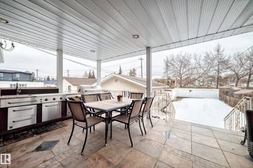 Covered outdoor patio area featuring tiled flooring, a built-in outdoor kitchen with stainless steel appliances, and a dining table with chairs - 12131 101 Street Nw, Edmonton, AB - Outdoor