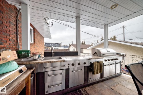 Outdoor kitchen area featuring a built-in stainless steel grill, a sink, and stone countertops, all under a covered patio with a white paneled ceiling - 12131 101 Street Nw, Edmonton, AB -  With Exterior