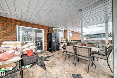 The property features an expansive covered patio with a brick wall and a sliding glass door - 12131 101 Street Nw, Edmonton, AB - Outdoor