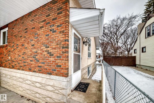 The property features a brick exterior with a patterned foundation, a covered entryway, and a side yard with a chain-link fence - 12131 101 Street Nw, Edmonton, AB - Outdoor With Exterior