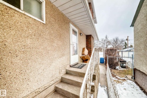 Exterior view featuring concrete steps with a white railing, a white door, and an exterior wall with a textured finish - 12131 101 Street Nw, Edmonton, AB - Outdoor With Exterior