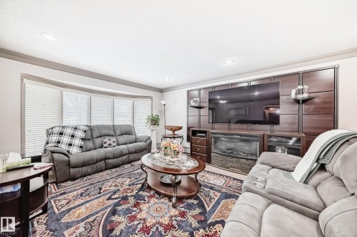 The living area features a bay window with blinds, recessed lighting, and a decorative fireplace with a stone facade - 12131 101 Street Nw, Edmonton, AB - Indoor Photo Showing Living Room With Fireplace
