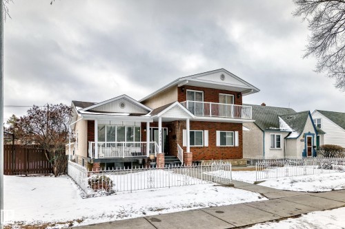 The property features a brick and stucco exterior, a second-floor balcony with white railings, and a covered porch with white railings - 12131 101 Street Nw, Edmonton, AB - Outdoor With Facade