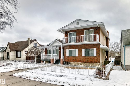The property features a brick and beige exterior, a front porch with white railings, and a second-story balcony - 12131 101 Street Nw, Edmonton, AB - Outdoor With Facade
