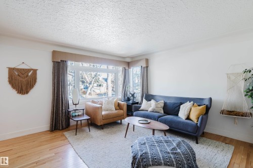 Living area featuring hardwood floors, a large window providing natural light, and a textured ceiling - 10643 66 Avenue, Edmonton, AB - Indoor Photo Showing Living Room