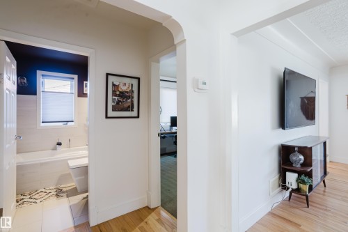 The property features a hallway with hardwood floors and an arched doorway, leading to a bathroom with a white tiled tub and a window with blinds - 10643 66 Avenue, Edmonton, AB - Indoor Photo Showing Other Room