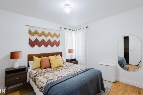 The property features hardwood floors, white walls, and a window with white curtains - 10643 66 Avenue, Edmonton, AB - Indoor Photo Showing Bedroom