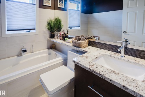 Contemporary bathroom featuring a white bathtub, a toilet, and a vanity with a white granite countertop and an integrated sink - 10643 66 Avenue, Edmonton, AB - Indoor Photo Showing Bathroom