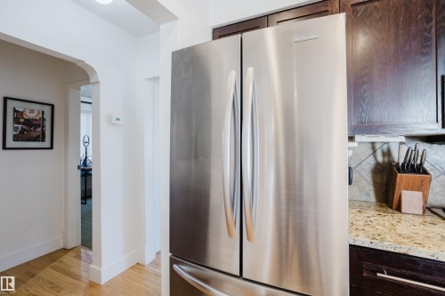 The kitchen features a stainless steel refrigerator, dark wood cabinetry, and a granite countertop - 10643 66 Avenue, Edmonton, AB - Indoor