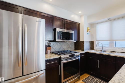 Kitchen featuring stainless steel appliances, dark wood cabinetry, granite countertops, and a tile backsplash - 10643 66 Avenue, Edmonton, AB - Indoor Photo Showing Kitchen With Upgraded Kitchen