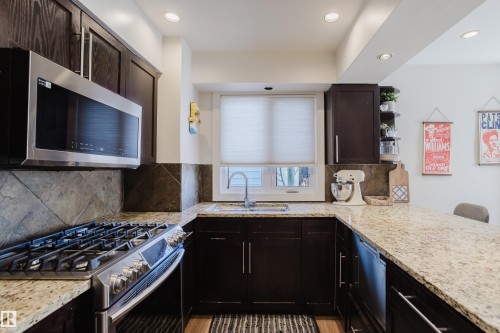 The kitchen features dark wood cabinetry, granite countertops, and a stainless steel oven with a gas cooktop - 10643 66 Avenue, Edmonton, AB - Indoor Photo Showing Kitchen
